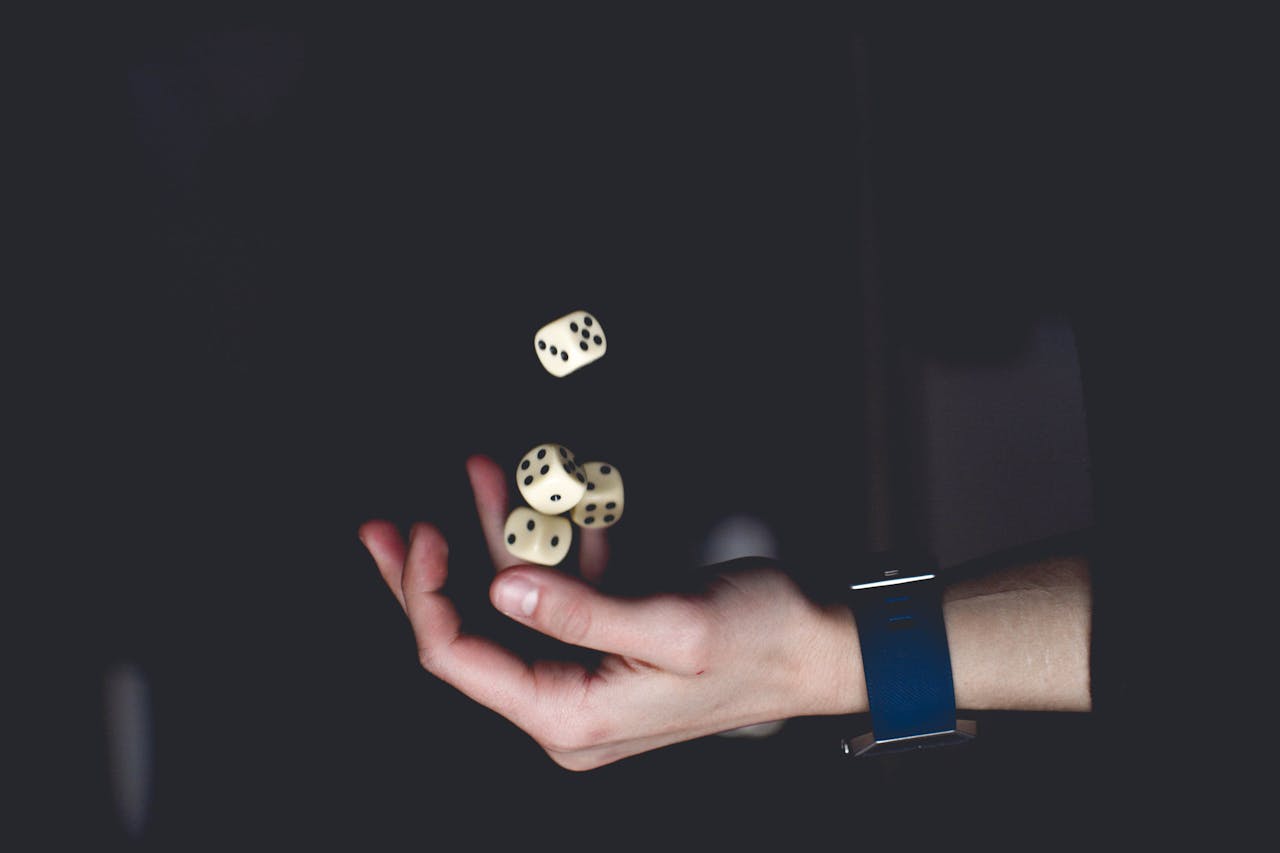 A close-up of a hand tossing several dice against a dark background, symbolizing chance and luck.