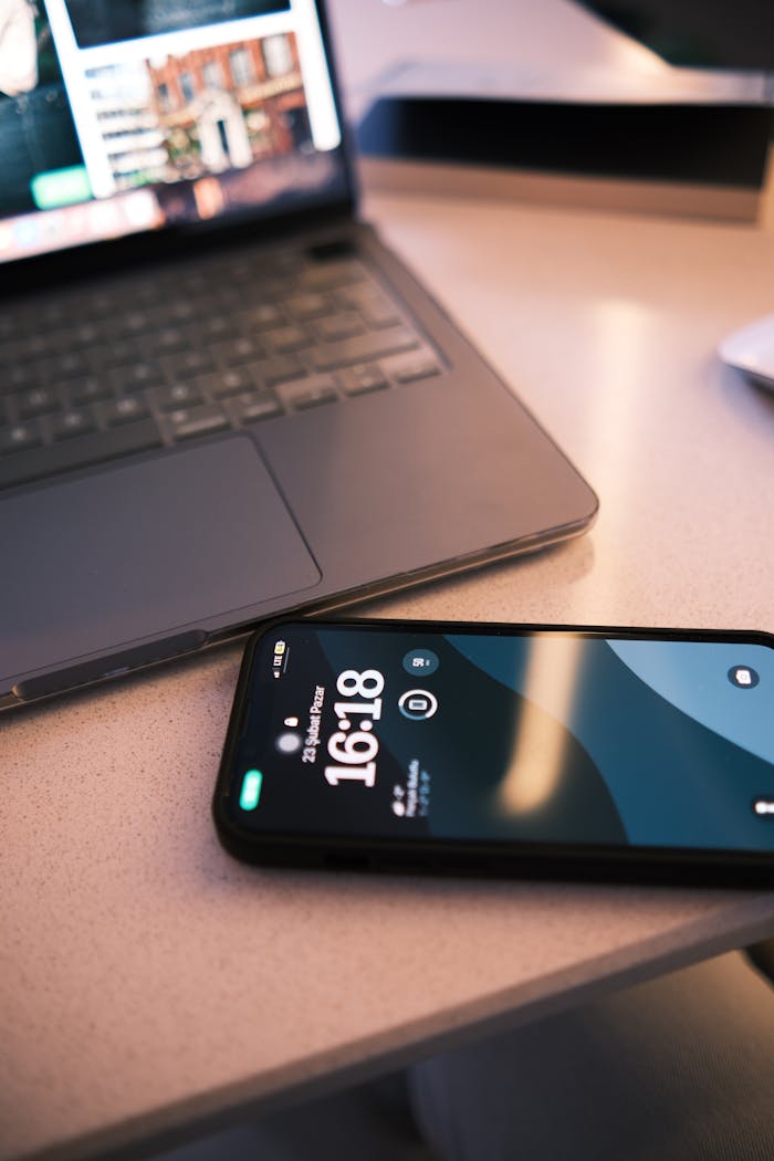 A sleek smartphone displaying time alongside a laptop on a desk, reflecting modern work life.